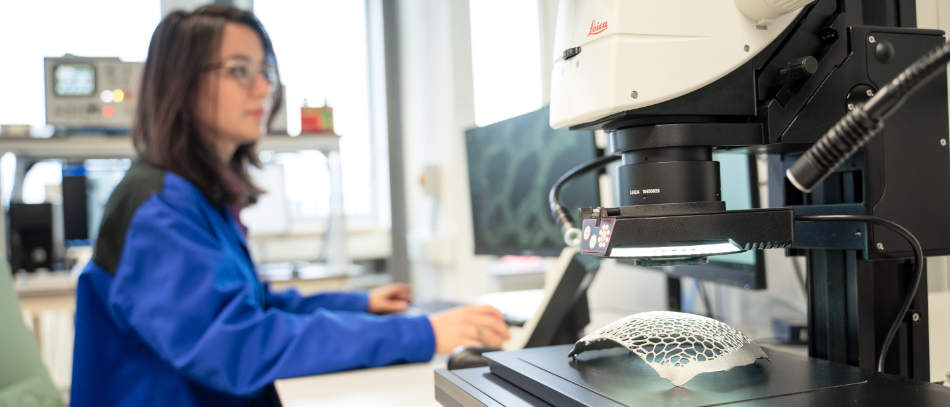 Ein Frau überprüft im Mikroskop einen 3D-Druck